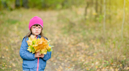 Happy young girl with Downs syndrom holds bouquet of autumn leaves. Empty space for text
