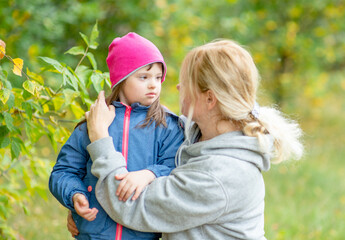 Mother and little girl with Down syndrom talk at autumn park