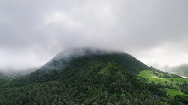 Drone shot of clouds and fog hanging over green Australian mountain with gumtrees