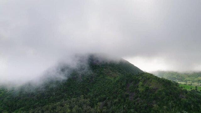 Drone shot of clouds and fog hanging over moody green Australian mountain with gumtrees