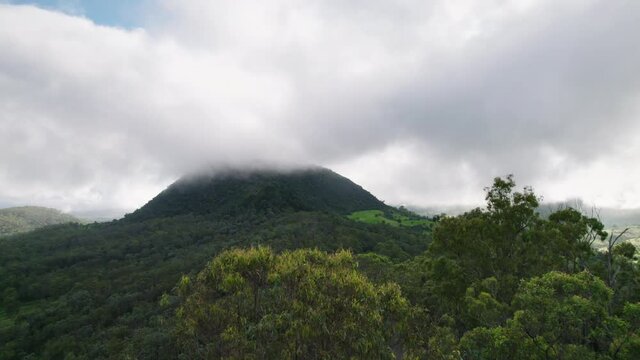 Drone shot past gumtrees revealing clouds and mist hanging over green Australian mountain
