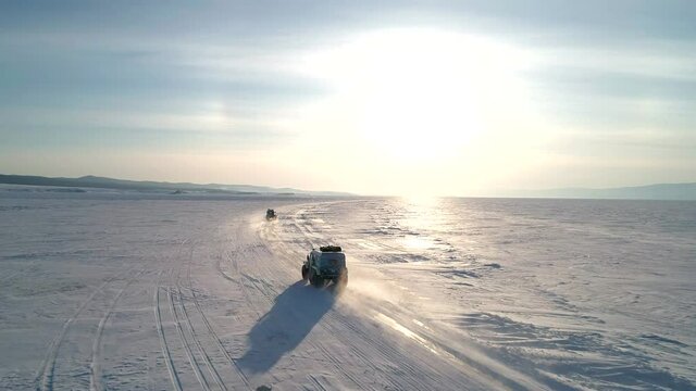 Aerial shot of off-roaders all-terrain vehicles SUV drive on snow and ice covered surface of Lake Baikal. Winter landscape. Popular tourist destination.