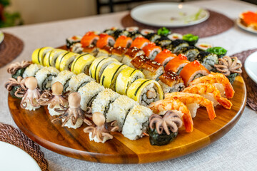Assortment of rolls and sushi on a wooden board on a festive table. Rolls with salmon, shrimps, omelette, octopus, crab, unagi. 