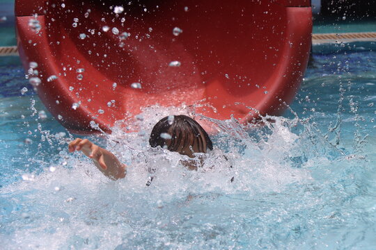 Young Asian Girl Splashing Into The Water At The End Of The Water Slide