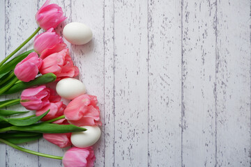 Easter concept floral background. Pink tulip flowers and eggs on white wooden table. Happy Easter background. 