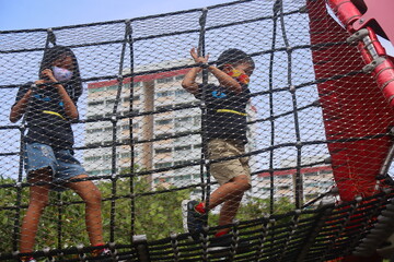 Asian children with masks at outdoor obstacle course playground against Singapore HDB backdrop