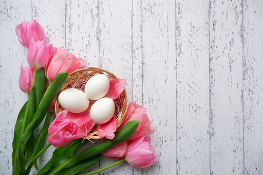 Easter concept floral background. Pink tulip flowers and eggs on white wooden table. Happy Easter background. 