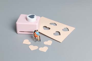 Miniature people Couple with with Heart shaped punching machine on gray background