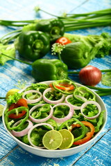 Bowl of delicious capsicum salad with onions, tomatoes and lime slice..