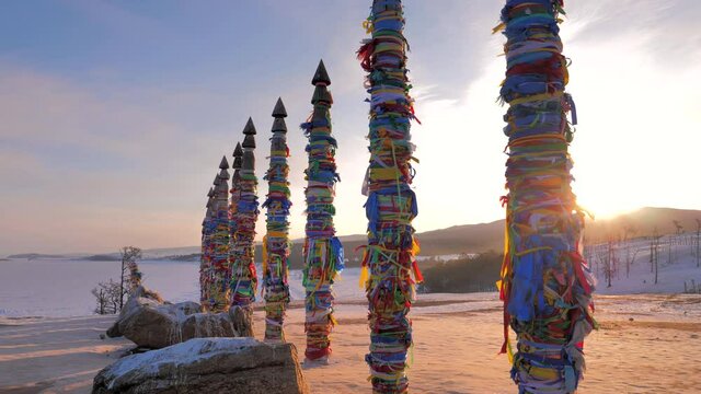 Sacred ritual pillars with colorful ribbons on cape Burkhan, Olkhon Island, lake Baikal at dawn on winter day.