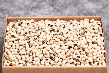 Pile of small raw white beans in a cardboard box on a gray stone background. Vegetarian food