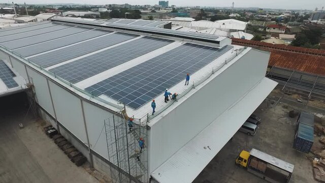 solar panel installation aerial view with men on scaffolding with warehouse roof being cleaned and prepared for aluminum attachments