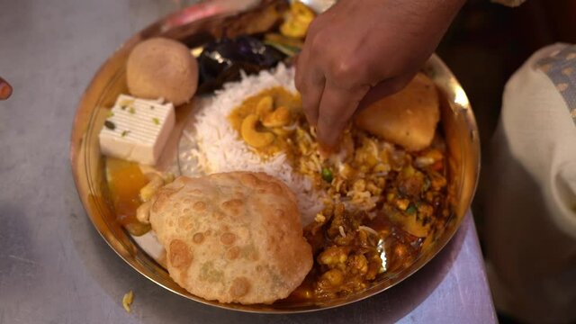 Smashing of Traditional Bengali dishes with hand for serving child during annoprashan or pooja festive food. A plate full of khichdi, pulao, curry, payesh and some fries