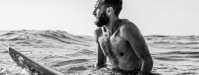 Horizontal banner or header with hipster surfer sitting on his surfboard into the ocean water and...