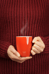 close-up woman in warm knitted sweater with red cup of hot drink.