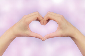Obraz premium female hands in the shape of a heart on a pink bokeh background.