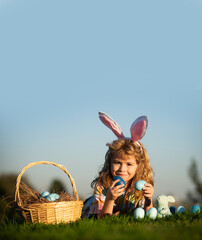 Child with easter eggs in basket outdoor. Boy laying on grass in park, on sky background with copy space. Easter egg hunt. Fynny kids portrait.