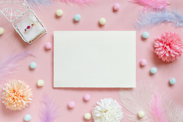 Blank card between pastel flowers, pom-poms and feathers near ring in a gift box on pink