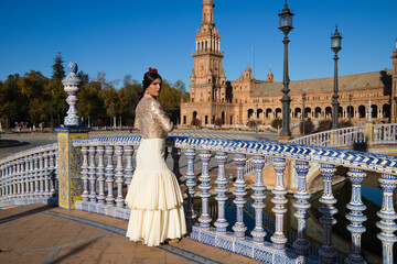 Fototapeta premium Flamenco dancer, woman, brunette and beautiful typical Spanish woman is looking at the camera leaning out of an Andalusian tiled railing. Flamenco concept of cultural heritage of mankind
