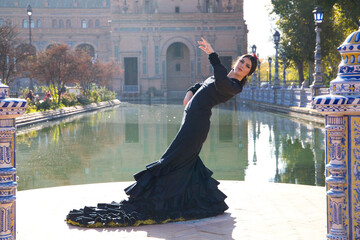 Woman dancing flamenco in black gypsy costume with yellow polka dots and red flower in her hair holding out her hands as she dances in the park in seville. flamenco cultural heritage of humanity.