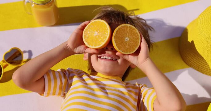 Happy child holding halves of orange fruit like a sunglasses. Slow motion