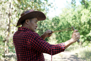 Asian man shooting a slingshot to shoot seeds into the forest Concept : Plant propagation in the...