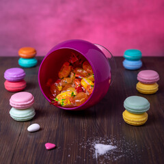 Composition of candies in an overturned glass container and pairs of superimposed colorful macarons
