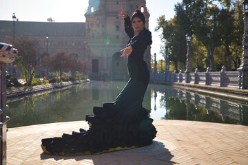 Young flamenco woman, Hispanic and brunette, with typical flamenco dance suit in black color and with tail, dancing with sun rays next to a lake. Concept of flamenco, dancer, typical Spanish dance. - obrazy, fototapety, plakaty