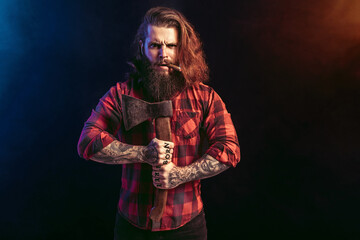 Handsome man with old axe. Bearded lumberjack. Serious brutal male in checkered shirt with long hair