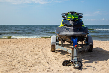 Black and green jet ski on a trailer on a sunny sandy beach of the seashore