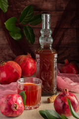 A still-life tableau of pomegranate fruits, a detailed glass bottle, and a refreshing juice-filled glass, surrounded by fresh green leaves on a rustic background.