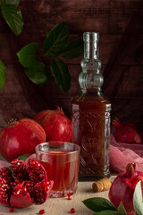 A rustic scene of fresh pomegranates, a crystal-clear bottle filled with pomegranate juice, and a glass of refreshing drink, framed by lush green leaves.