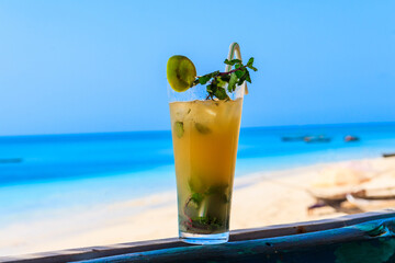 Glass of fresh orange mojito cocktail by the ocean