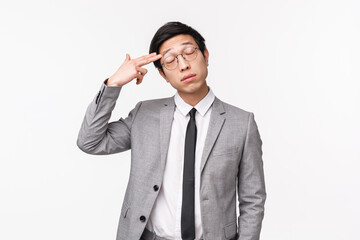 Waist-up portrait of annoyed and fed-up, tired asian guy in grey suit, close eyes and making gun...