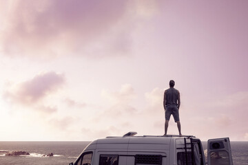 Man standing on top of a camper van next to the ocean