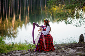 Young woman playing harp at the lake - obrazy, fototapety, plakaty