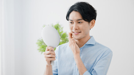 ハンドミラーで肌をチェックする若い男性　スキンケア