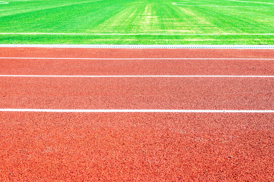 Side view of a running track in a stadium and part of a soccer field with green artificial turf. Background, copy space