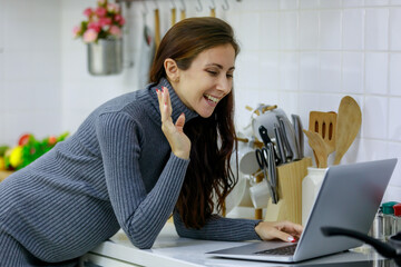 Caucasian millennial young happy sexy female prenatal pregnant mother in casual gray pregnancy dress standing smiling using fork eating grape and fruits in kitchen while surfing internet via laptop