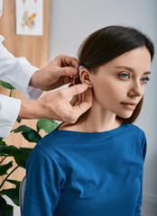 Caucasian woman during installation hearing aid into her ear by her audiologist, close-up. Hearing...