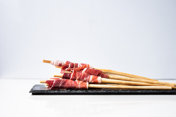 Slices of acorn-fed Iberian ham with breadsticks, Spanish tapa, for events, dinners or celebrations, on a black slate