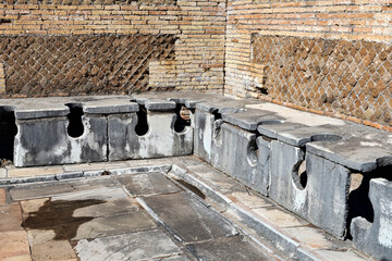 Well-preserved remains of an ancient Roman public bathroom with travertine seats and toilet drains, under the seats, the drains were constantly cleaned by a path of rough water