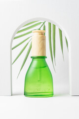 Green dropper bottle on white background with tropical palm leaf. Blank aromatic oil container design, medical packaging template. Herbal cosmetic concept. Trendy showcase with podium and greenery