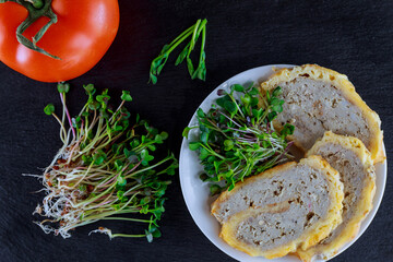 Microgreens of cabbage and peas and meat rolls in a white plate and tomato on a black background.