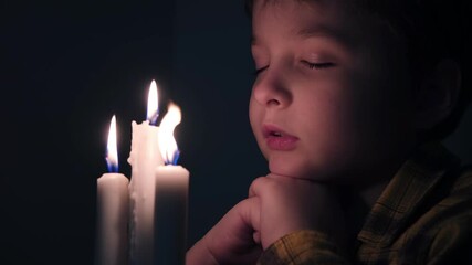 Little cute boy reads a prayer in the dark with a candle - Powered by Adobe
