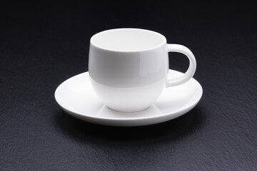 Empty white coffee cup with saucer on a black background.