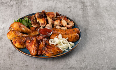 Assorted grilled meat in a plate on the table. Fried chicken legs and wings, sausages, shish kebab, pickled onions and tomato sauce. Horizontal orientation, copy space, no people