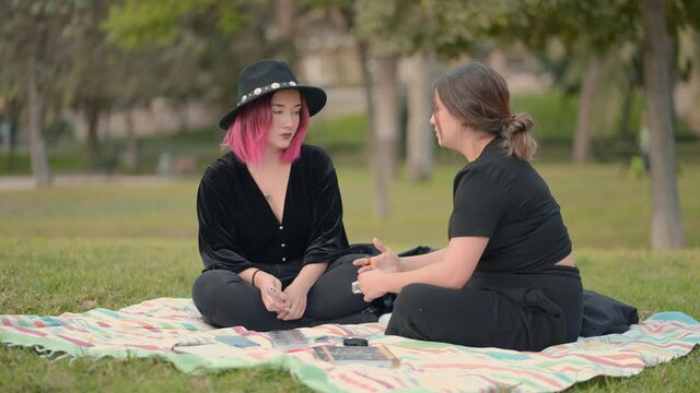 caucasian girls dialoguing while sitting on the grass in the park. wide view