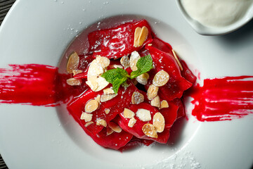 Classic Ukrainian Pierogi or Varenyky with cherries, red sauce, sour cream and almonds in a white...