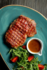 Beef steak with salad and honey sauce in a blue plate. Wood background